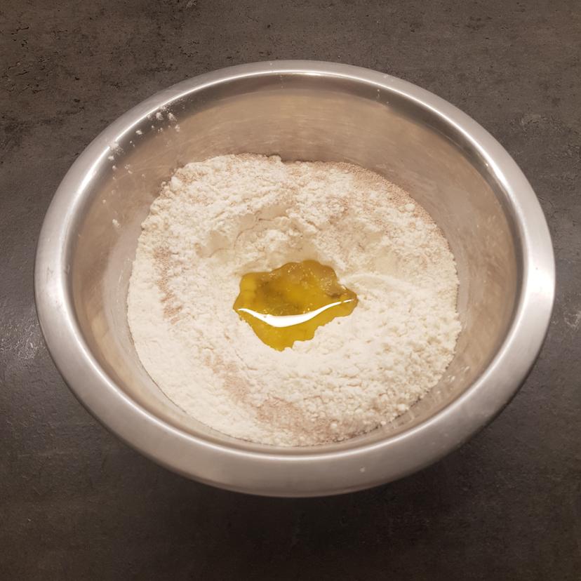 Farine, levure et sel dans un saladier. Puits formé et huile d'olive ajouté