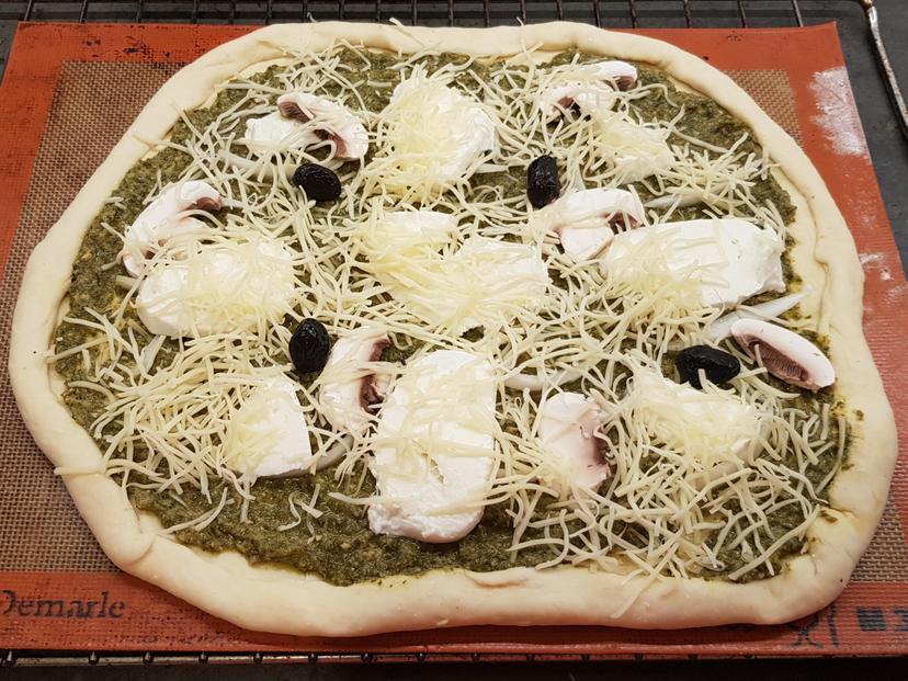 Pizza avec la garniture : pesto, mozzarella, champignons, gruyère, olives avant cuisson 