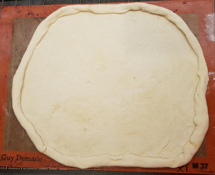 Pâte à pizza étalé avec bords délimités sur une plaque de cuisson 